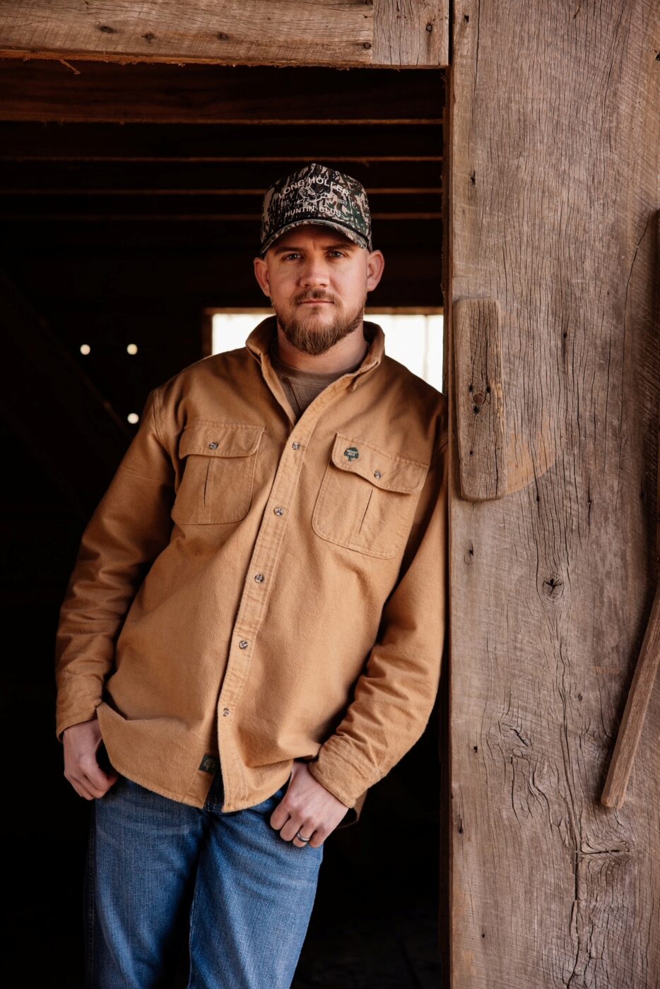 Drew Parker wears a tan shirt and camouflage cap beside a wooden post.