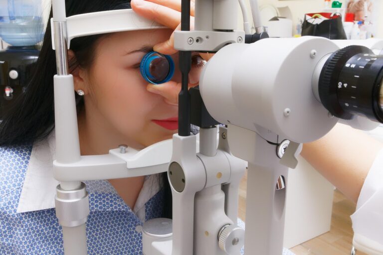 A child looks into an eye exam machine while a clinician adjusts the equipment.