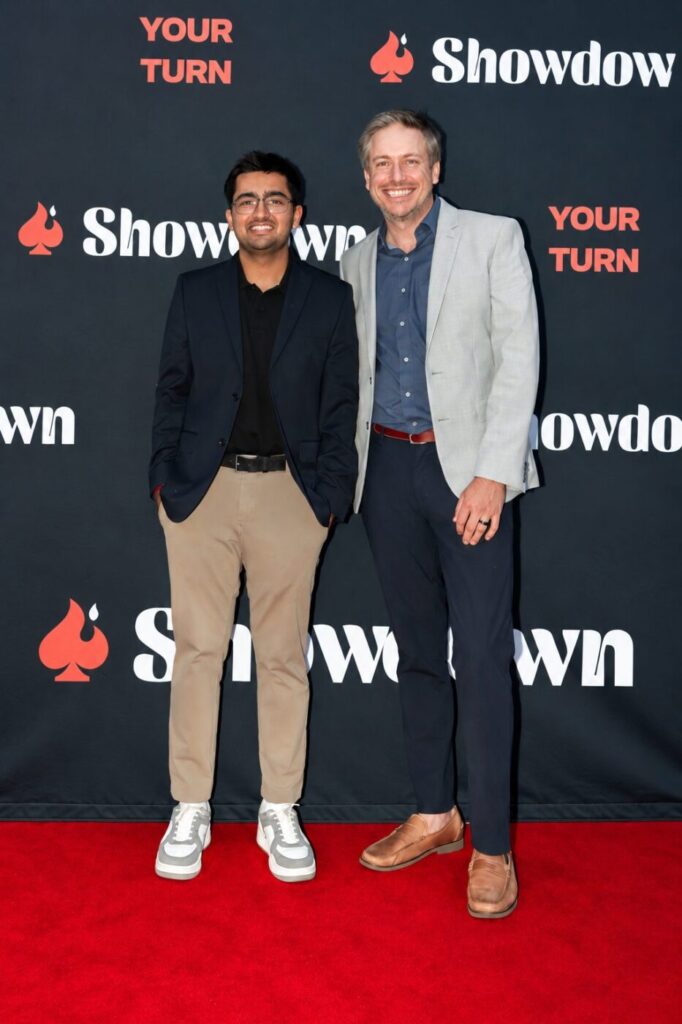 Two men stand in front of a Showdown backdrop on a red carpet.