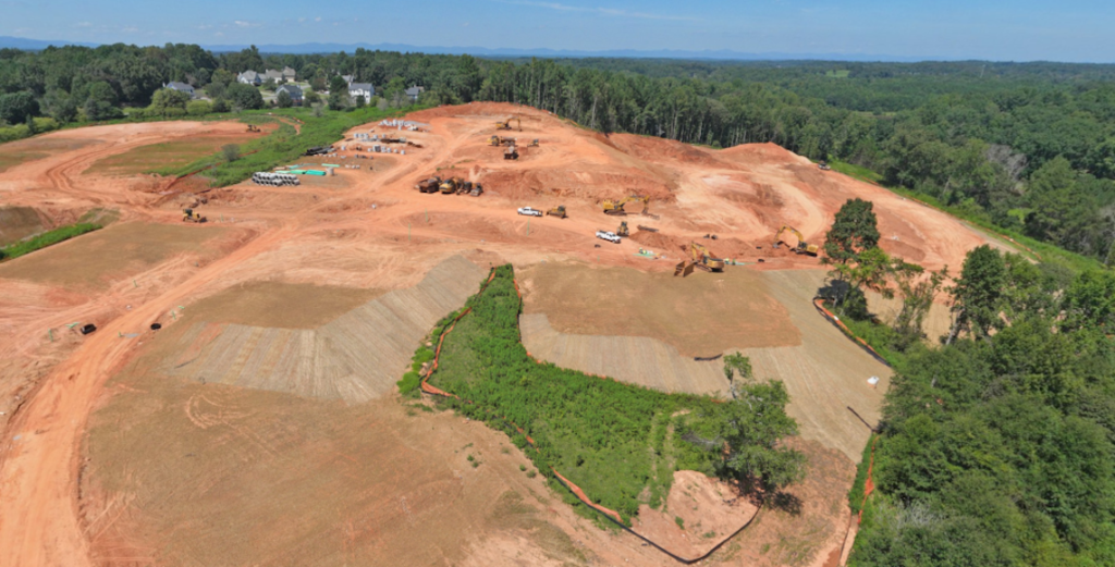 Aerial view of a large graded construction site surrounded by trees.