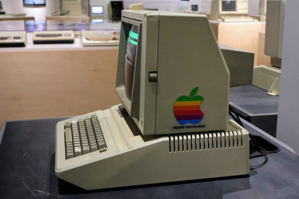 An early Apple computer sits in a museum case with its keyboard attached.
