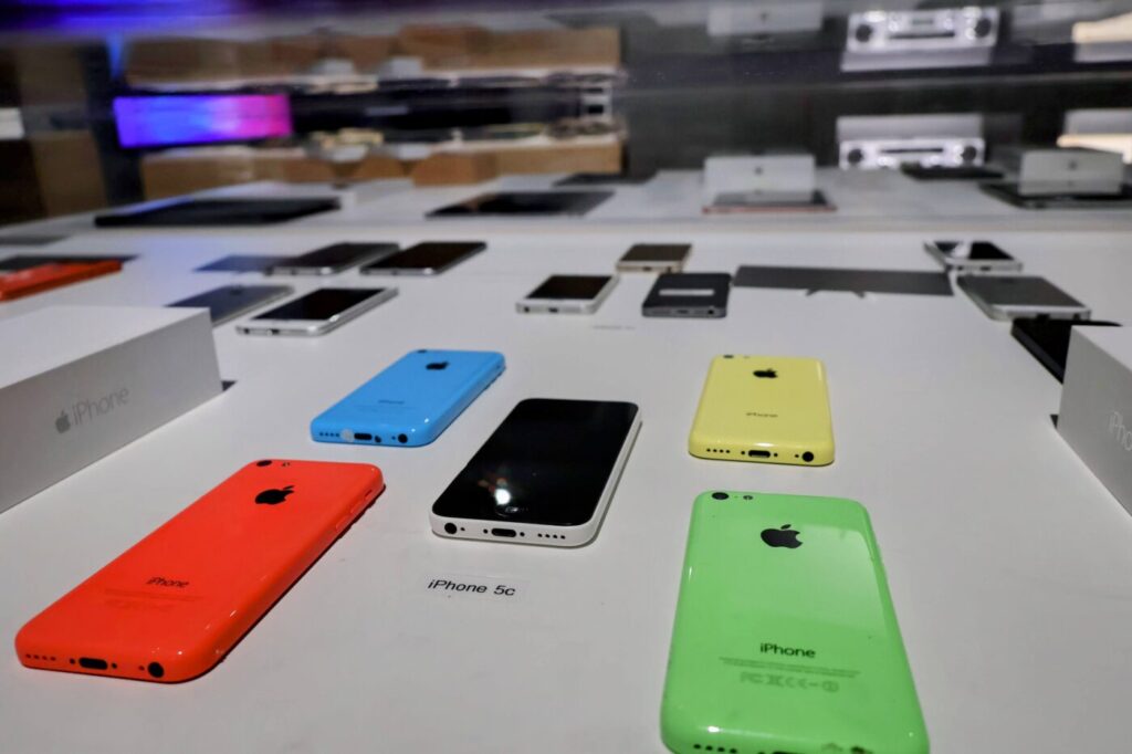 Colorful iPhone models are displayed on a white surface in a museum exhibit.