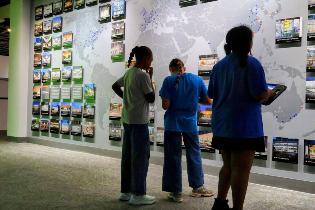 Three students look at a wall map covered with exhibit photos and location markers.