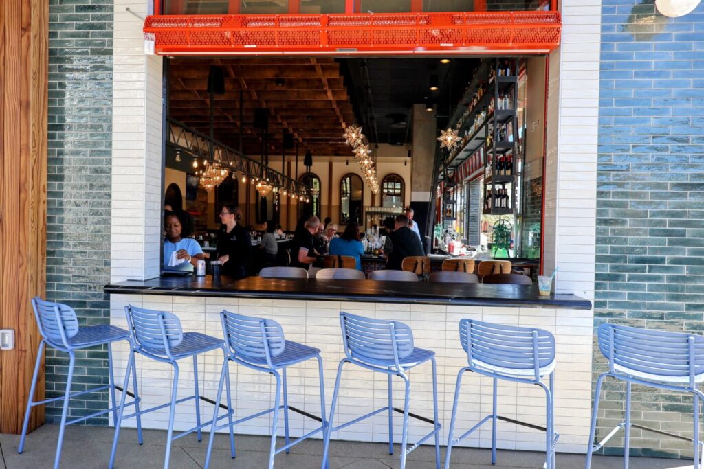 Blue stools lined up at an outdoor counter by an open window