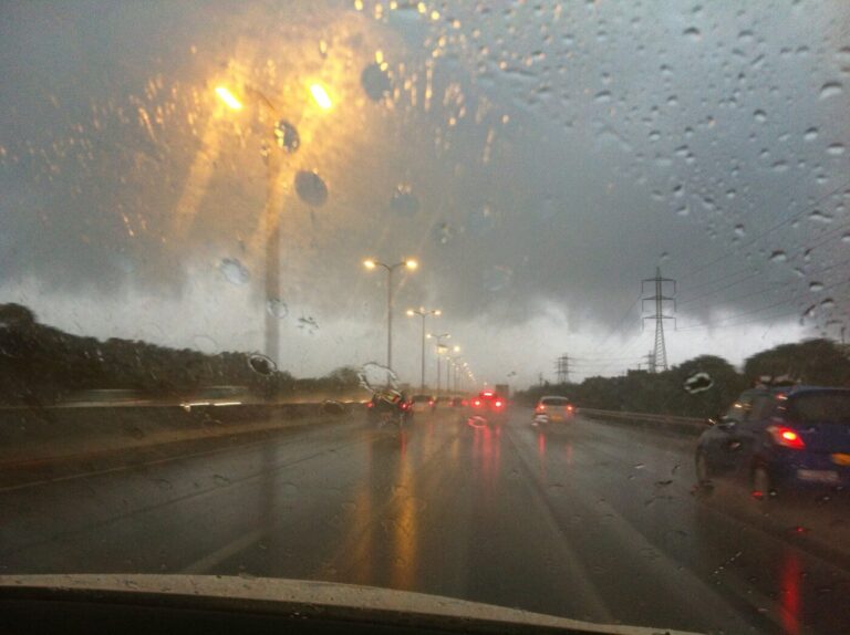 Cars drive on a wet highway in heavy rain with dark storm clouds ahead.
