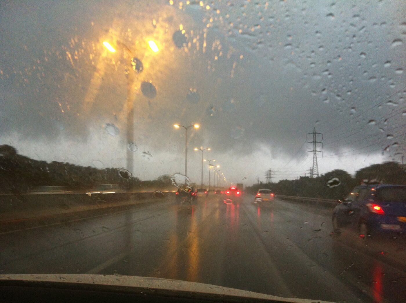 Cars drive on a wet highway in heavy rain with dark storm clouds ahead.