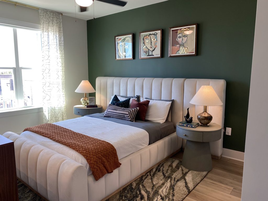 Bedroom at Prelude in Medley, with a cream upholstered bed, dark green accent wall, framed portraits and matching bedside lamps.