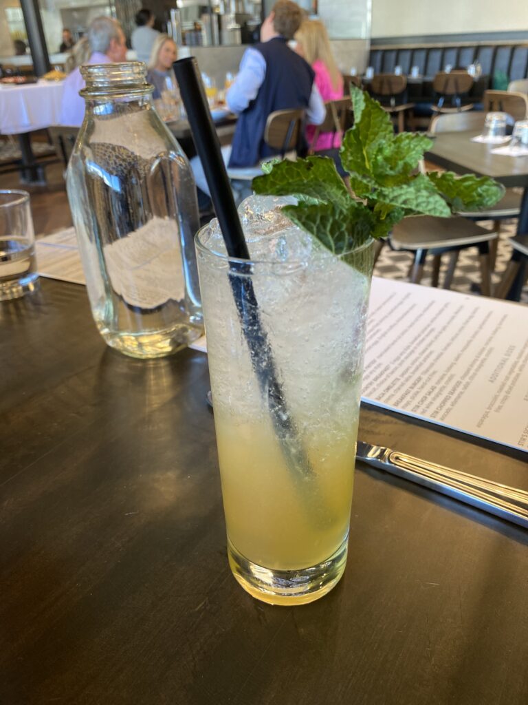 Tall pale-yellow drink with mint on top and a straw on the table