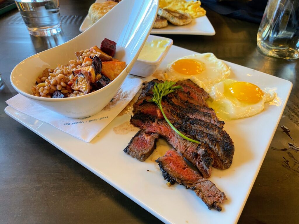 Slice of steak with two sunny-side-up eggs and a side bowl of grains and vegetables