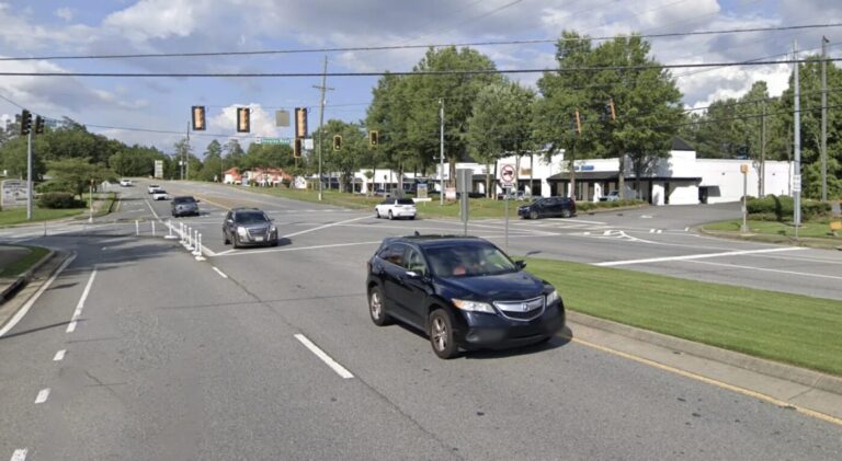 Cars travel along Jones Bridge Road near a signalized intersection with a grassy median and utility lines overhead.
