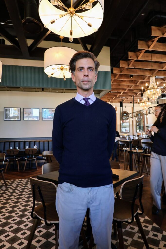 Man standing inside the restaurant beneath large pendant lights