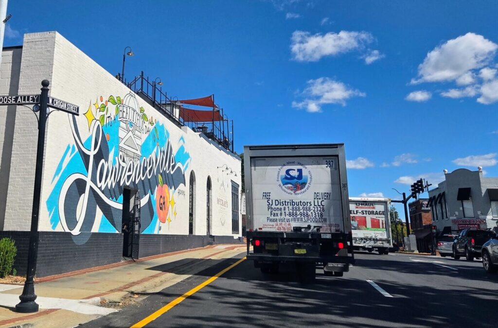 A delivery truck drives past a Lawrenceville mural on a sunny street.