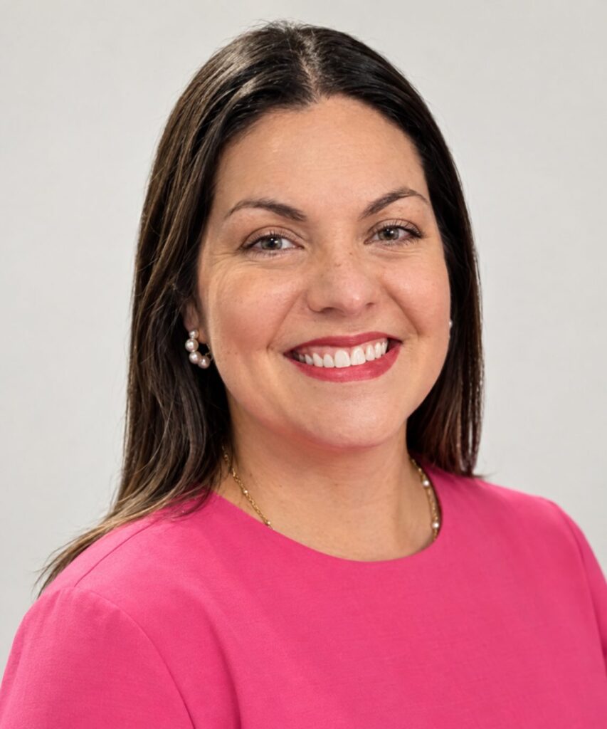 A smiling woman in a bright pink top poses against a light gray background.