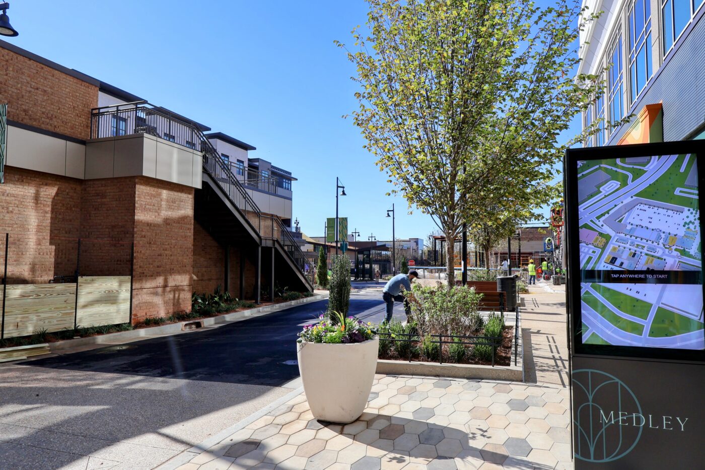 Medley directory beside a flower-filled planter and tree-lined street with an exterior staircase.