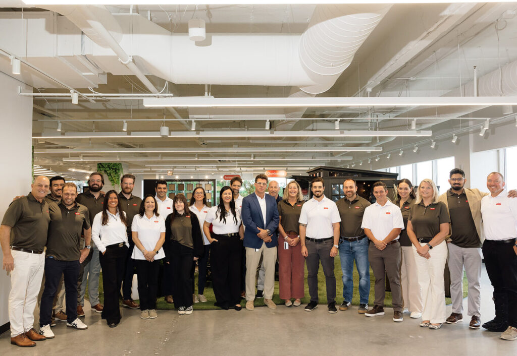 A group of people poses inside a bright showroom with exposed ceiling ducts and product displays in the background.