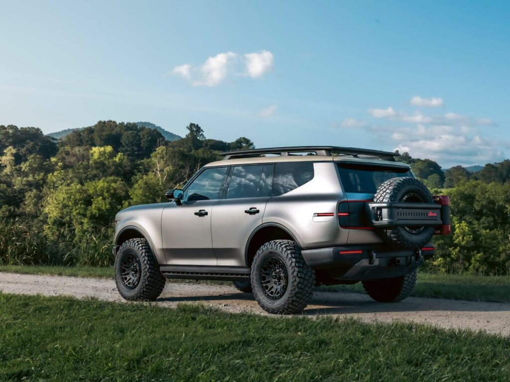 A silver Scout SUV on a dirt road with trees and hills in the background