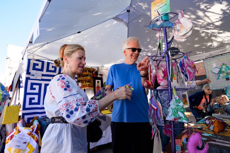 A woman and a man browse handmade crafts under a festival tent.