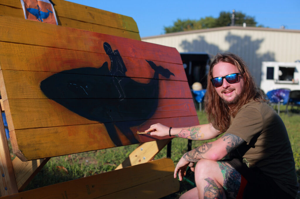 An artist paints a wooden panel at the 2025 Not Your Mother’s Art Fest.