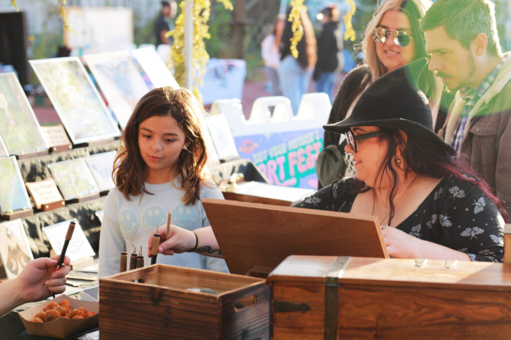 Children and adults gather around an art activity table at the 2025 Not Your Mother’s Art Fest.