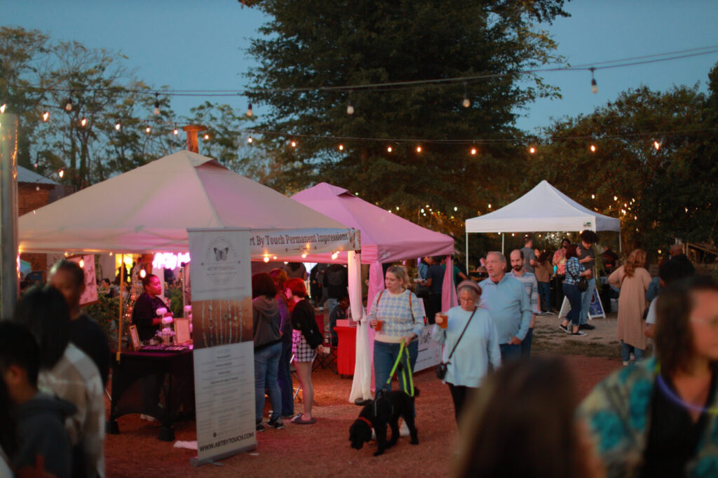 Crowd moves through an evening art market under string lights and tents.