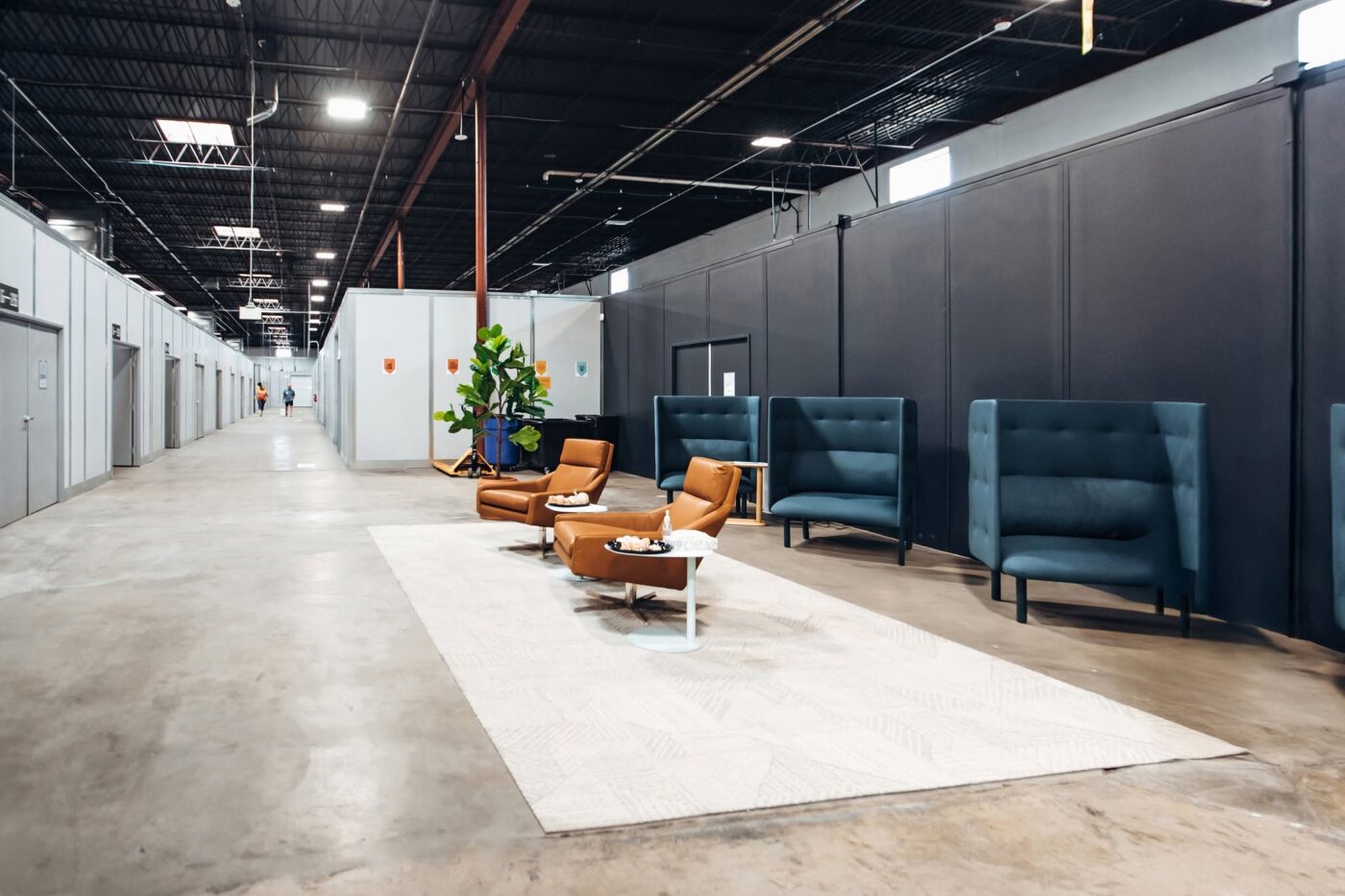 Warehouse corridor with private suite doors, lounge chairs and small tables on a light rug.