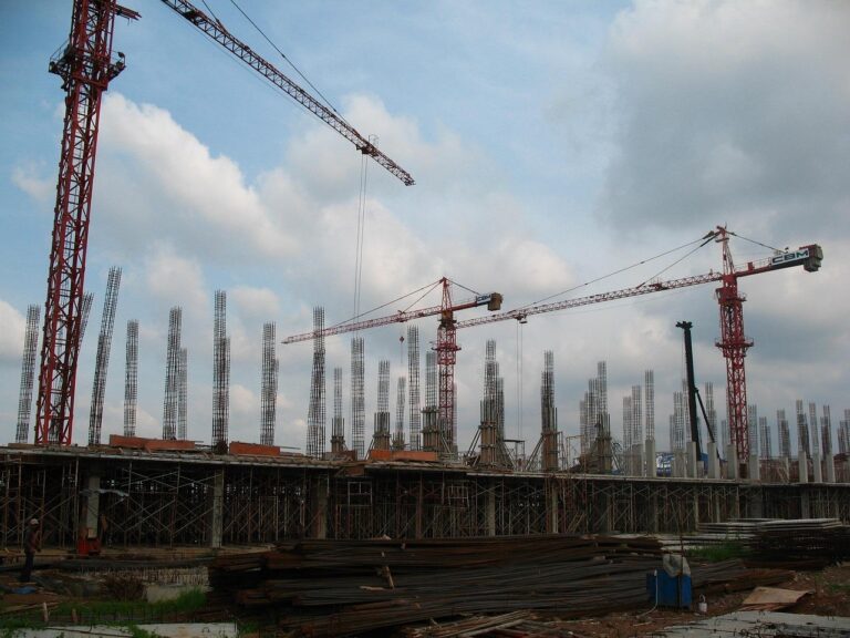 Construction site with several tower cranes and rows of concrete columns under a cloudy sky.