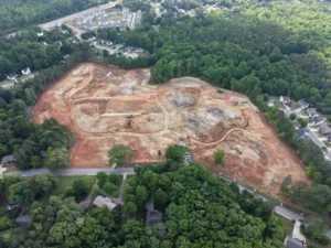Aerial view of a cleared construction site surrounded by trees and nearby homes
