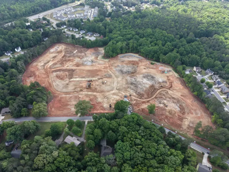 Aerial view of a cleared construction site surrounded by trees and nearby homes