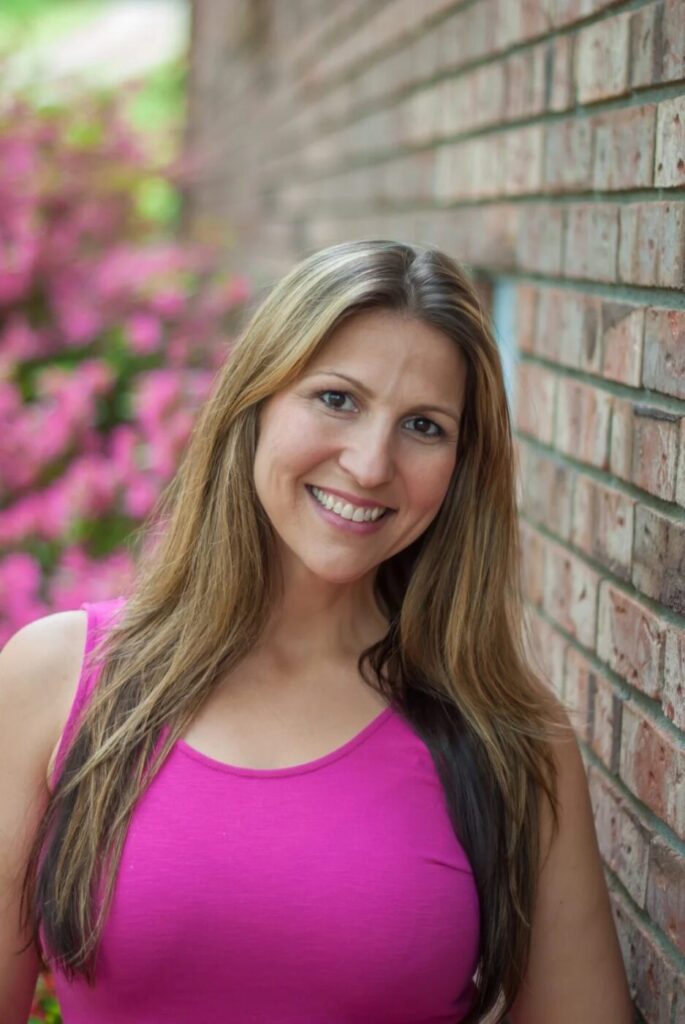 Serra Deville, founder and owner of Dream Nannies, standing beside a brick wall.