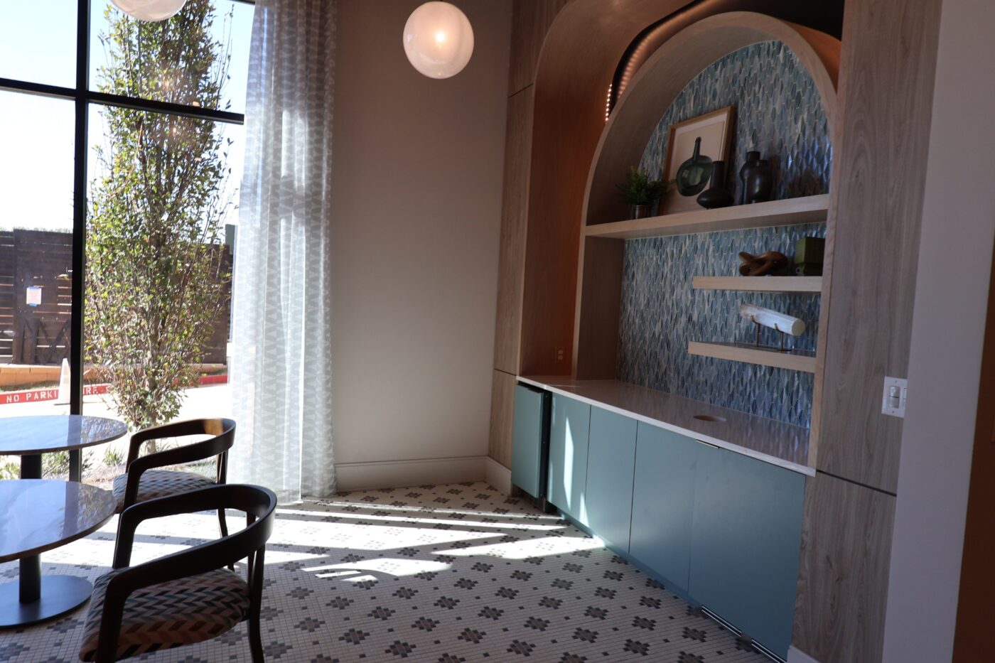 Small tables beside a window and arched shelving with blue-green cabinets at Prelude.