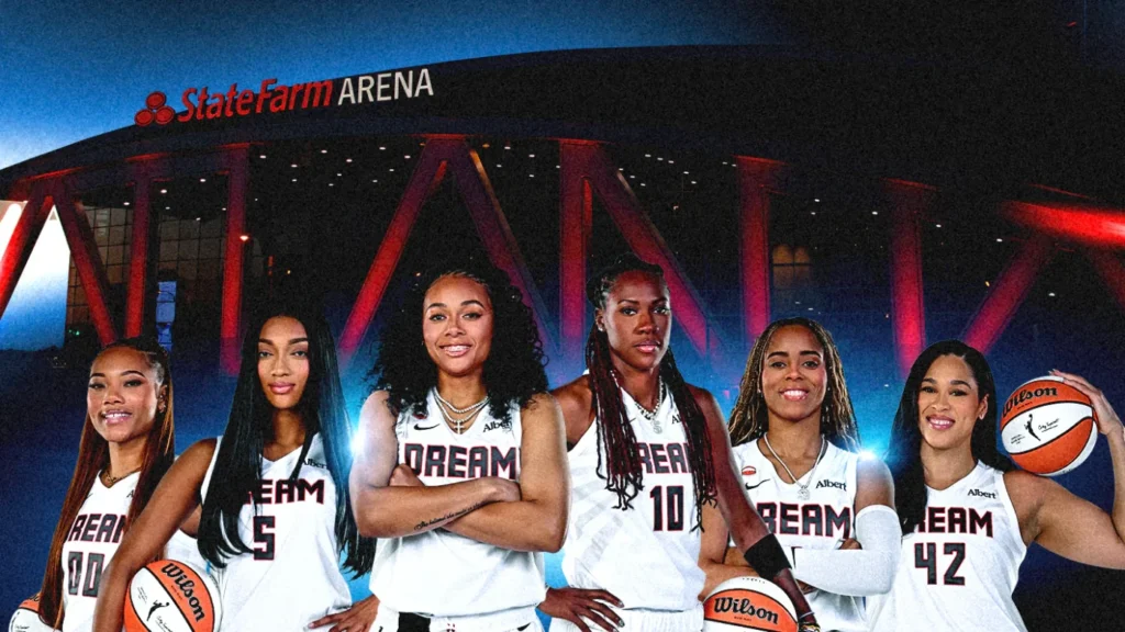 Six Atlanta Dream players stand in front of State Farm Arena at night, wearing white uniforms and holding basketballs.