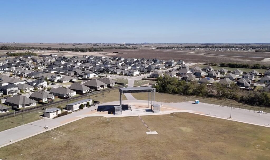 Aerial view of a suburban neighborhood with rows of houses and open land beyond