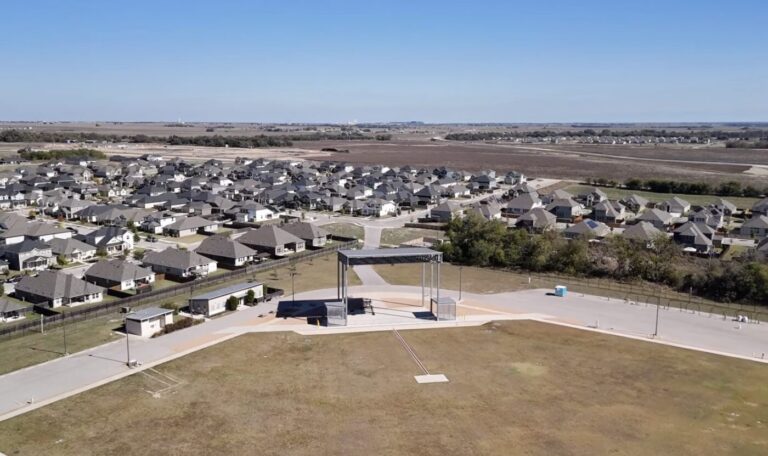 Aerial view of a suburban neighborhood with rows of houses and open land beyond