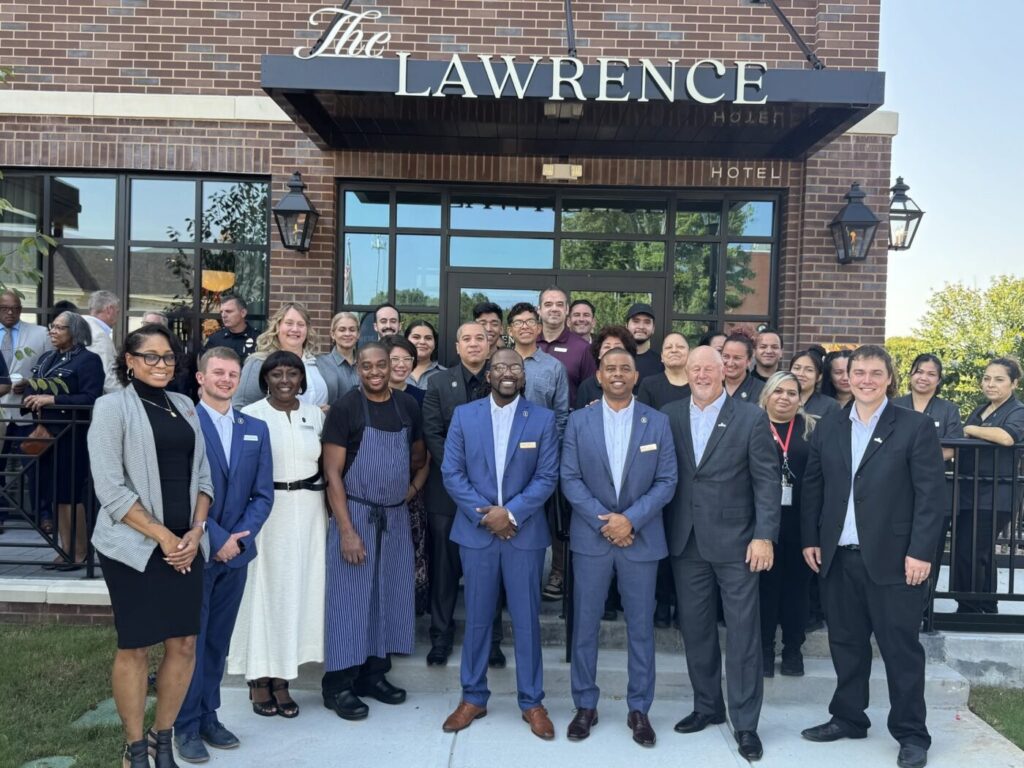 A group of people stands outside The Lawrence Hotel entrance under a black awning.