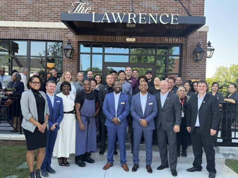 A group of people stands outside The Lawrence Hotel entrance under a black awning.