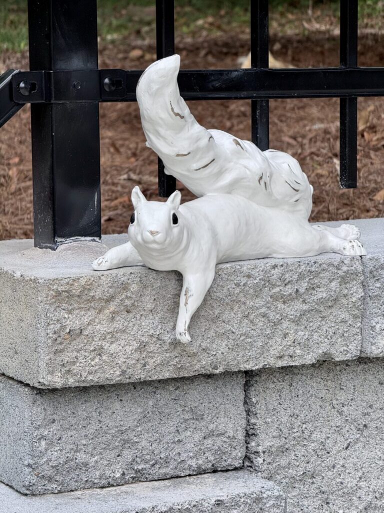 A white squirrel sculpture reclines on a stone ledge in front of black metal railings.