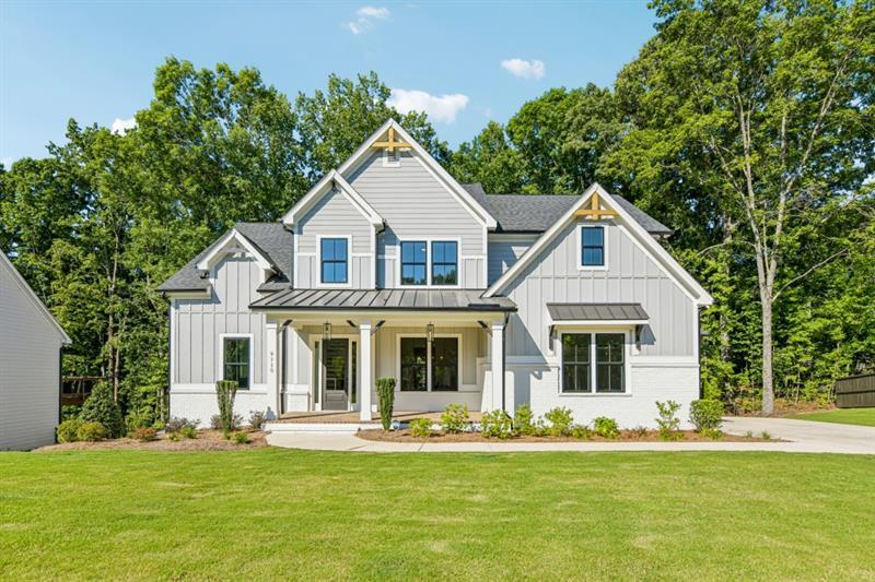 A white two-story house with black roof accents, a covered front porch, and a green lawn in front of trees.