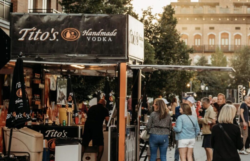 Festivalgoers stand near a Tito's Handmade Vodka booth and outdoor vendor tents in downtown Alpharetta.