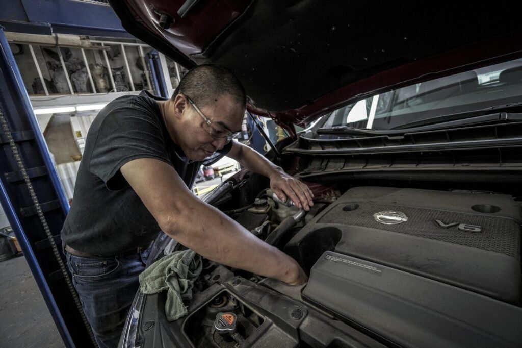 A mechanic leans over the open hood of a vehicle inside a repair shop.
