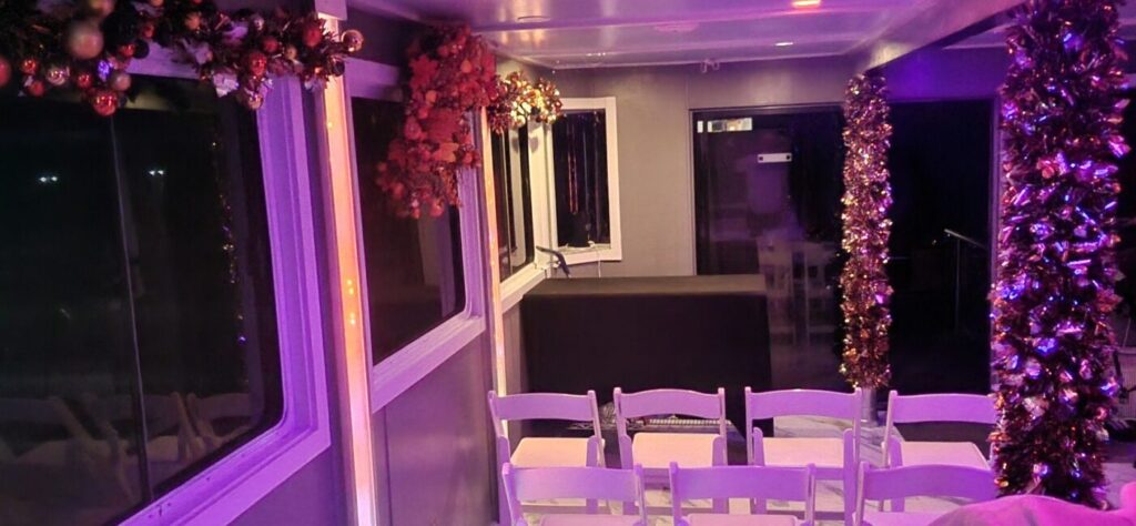 A decorated boat cabin with white chairs, windows and purple lighting
