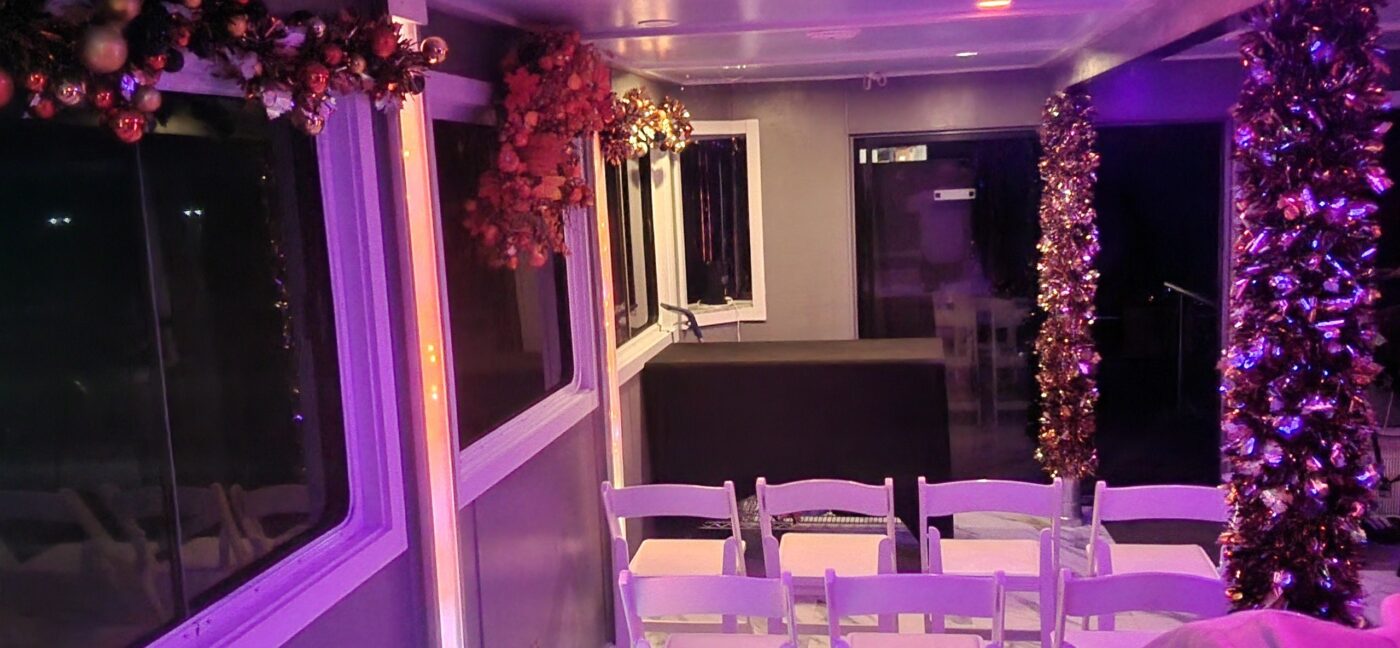 A decorated boat cabin with white chairs, windows and purple lighting