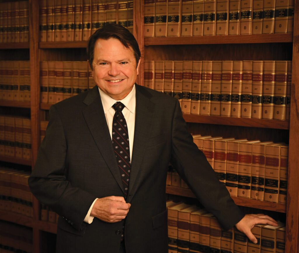 A man in a dark suit stands before shelves of law books, smiling at the camera.