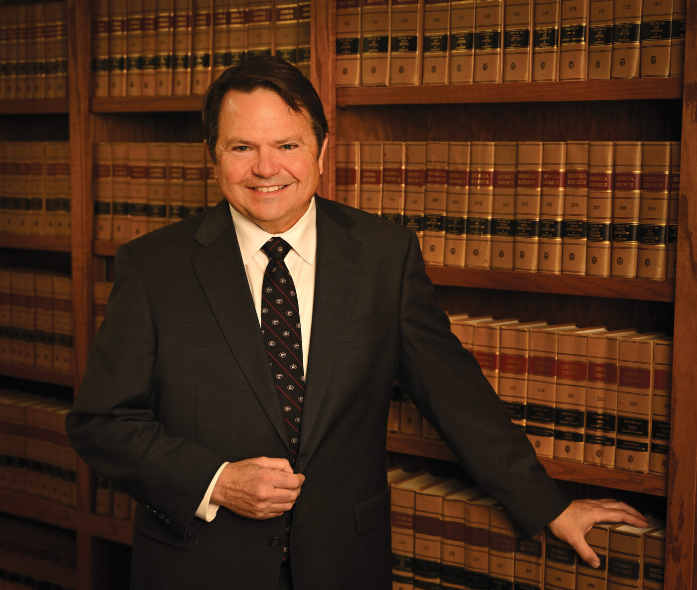 A man in a dark suit stands before shelves of law books, smiling at the camera.
