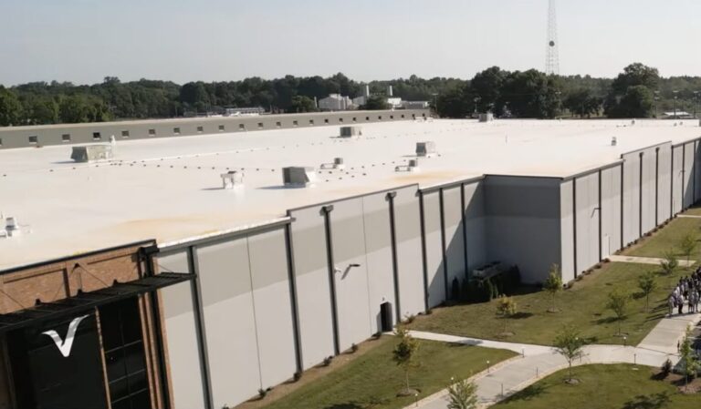 A large white industrial building with a flat roof and landscaped walkway along the side.