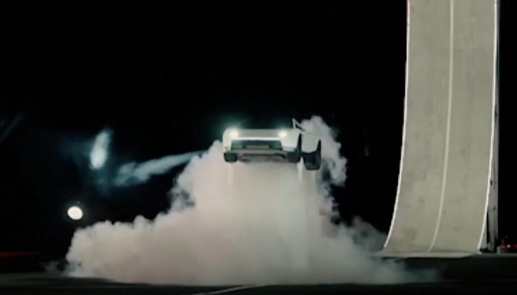 A car lifts off the ground beside a large vertical structure, surrounded by smoke at night.